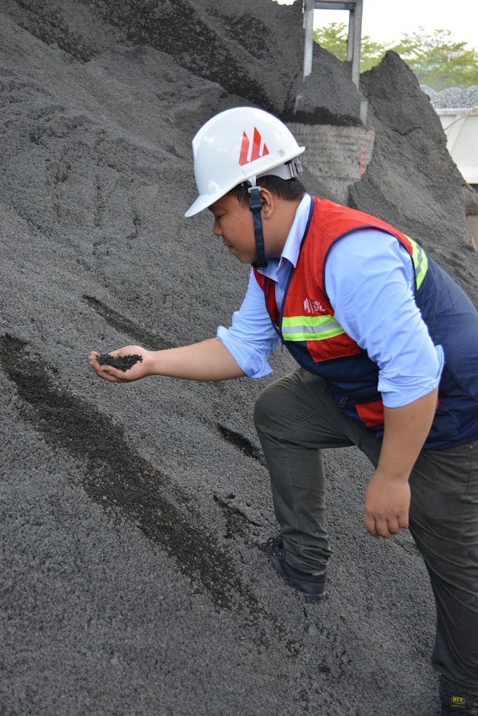 Construction worker examining a pile of material at a work site outdoors in daylight.